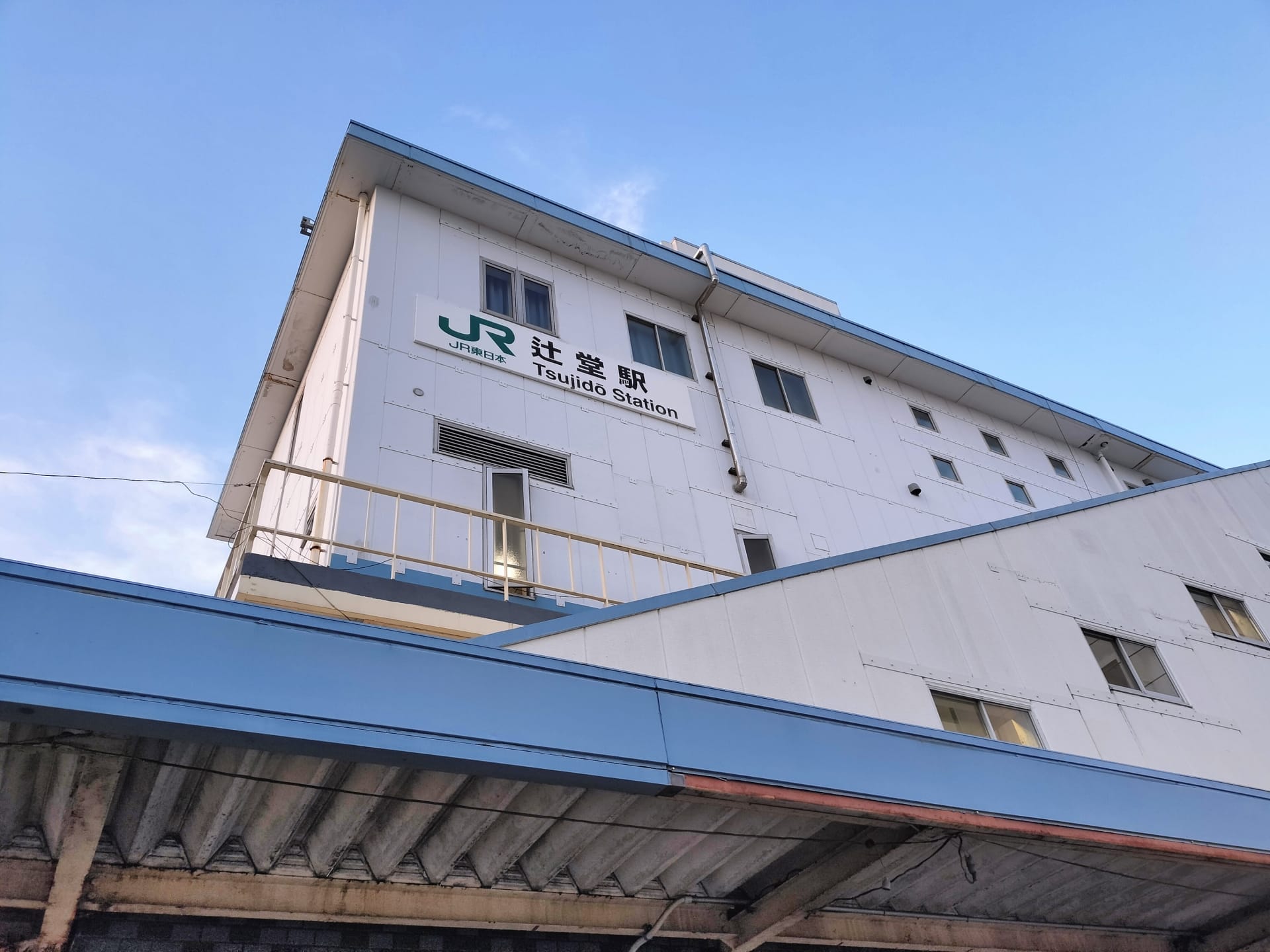 辻堂にある辻堂駅舎の外観。澄み切った青空の下、白い壁に駅名とJRのロゴが優雅に表示されている。.