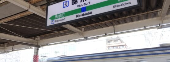 錦糸町駅のホームを電車が通り過ぎると、人気の錦糸町地区のすぐそばにある馬喰町と新小岩方面への案内標識が立っている。.