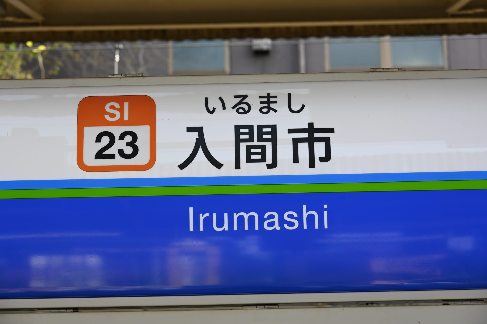 駅の標識には、駅コード SI 23 とともに、英語と日本語の両方で「入間市」と大きく表示されています。.