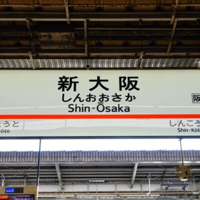 駅の標識には日本語と英語で「Shin-Osaka」と「新大阪」と表示されており、矢印は京都と新神戸を指している。.