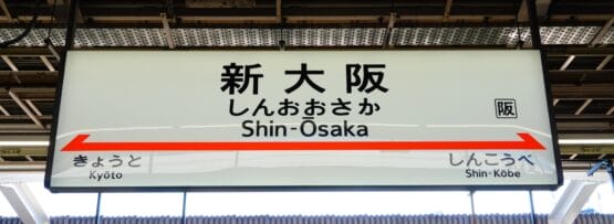 駅の標識には日本語と英語で「Shin-Osaka」と「新大阪」と表示されており、矢印は京都と新神戸を指している。.