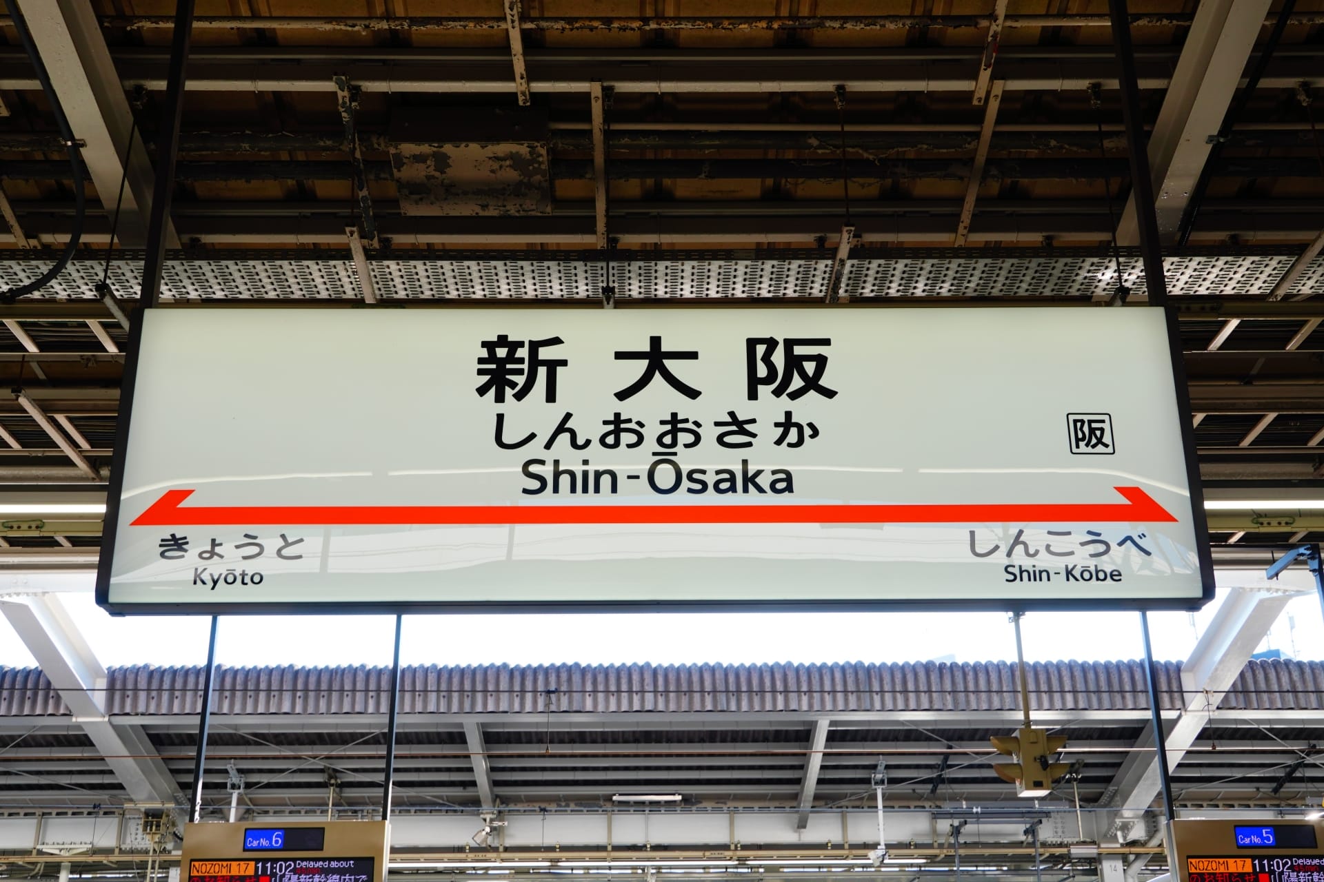 駅の標識には日本語と英語で「Shin-Osaka」と「新大阪」と表示されており、矢印は京都と新神戸を指している。.