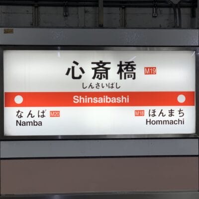 地下鉄の駅看板には「心斎橋」と「難波」（M20）と「本町」（M18）への行き方が日本語と英語で表示されており、地元の観光スポットや近くの韓国語教室マンツーマンなどの韓国語教室を探している旅行者に最適です。.