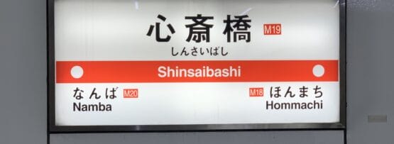 地下鉄の駅看板には「心斎橋」と「難波」（M20）と「本町」（M18）への行き方が日本語と英語で表示されており、地元の観光スポットや近くの韓国語教室マンツーマンなどの韓国語教室を探している旅行者に最適です。.