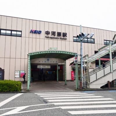 ベージュ色の外観と KEIO の看板が目印の中原駅の入り口には、手前に歩道と横断歩道へと続く階段があります。近くには、マンツーマンで学べる韓国語の個別クラスがあります。.