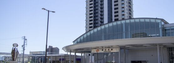 春日井の近代的な鉄道駅の入り口は、澄み切った青空の下の高層ビル群を背景に、洗練されたガラスのファサードと屋根付きの通路を誇っています。.