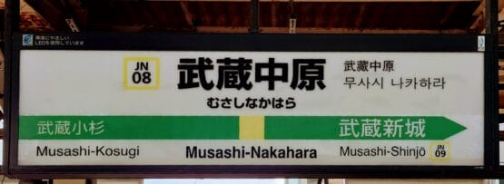 駅名標には武蔵中原（武蔵中原）を中心に、武蔵小杉と武蔵新城への方向が表示されています。標識には日本語、英語で書かれ、言語学習者向けに韓国語教室マンツーマンへの敬意が示されています。.