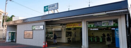 JR 西日暮里駅入口の外観。標識、改札口、駅に入る 2 人の人物。おそらく近くの韓国語教室マンツーマンに個別の言語レッスンを受ける途中だろう。.