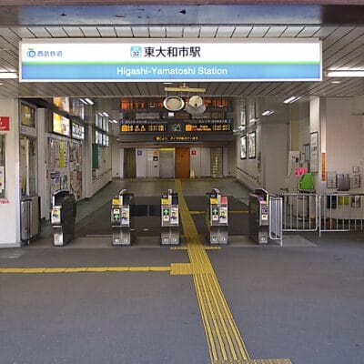 東大和市の東大和市駅の入口には、複数の改札口、標識、その上にある照明付きの出発案内板があり、韓国語教室のマンツーマン環境に見られる合理的な効率性を思い出させます。.