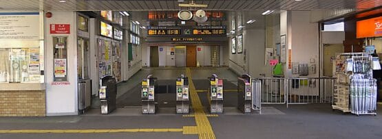 東大和市の東大和市駅の入口には、複数の改札口、標識、その上にある照明付きの出発案内板があり、韓国語教室のマンツーマン環境に見られる合理的な効率性を思い出させます。.