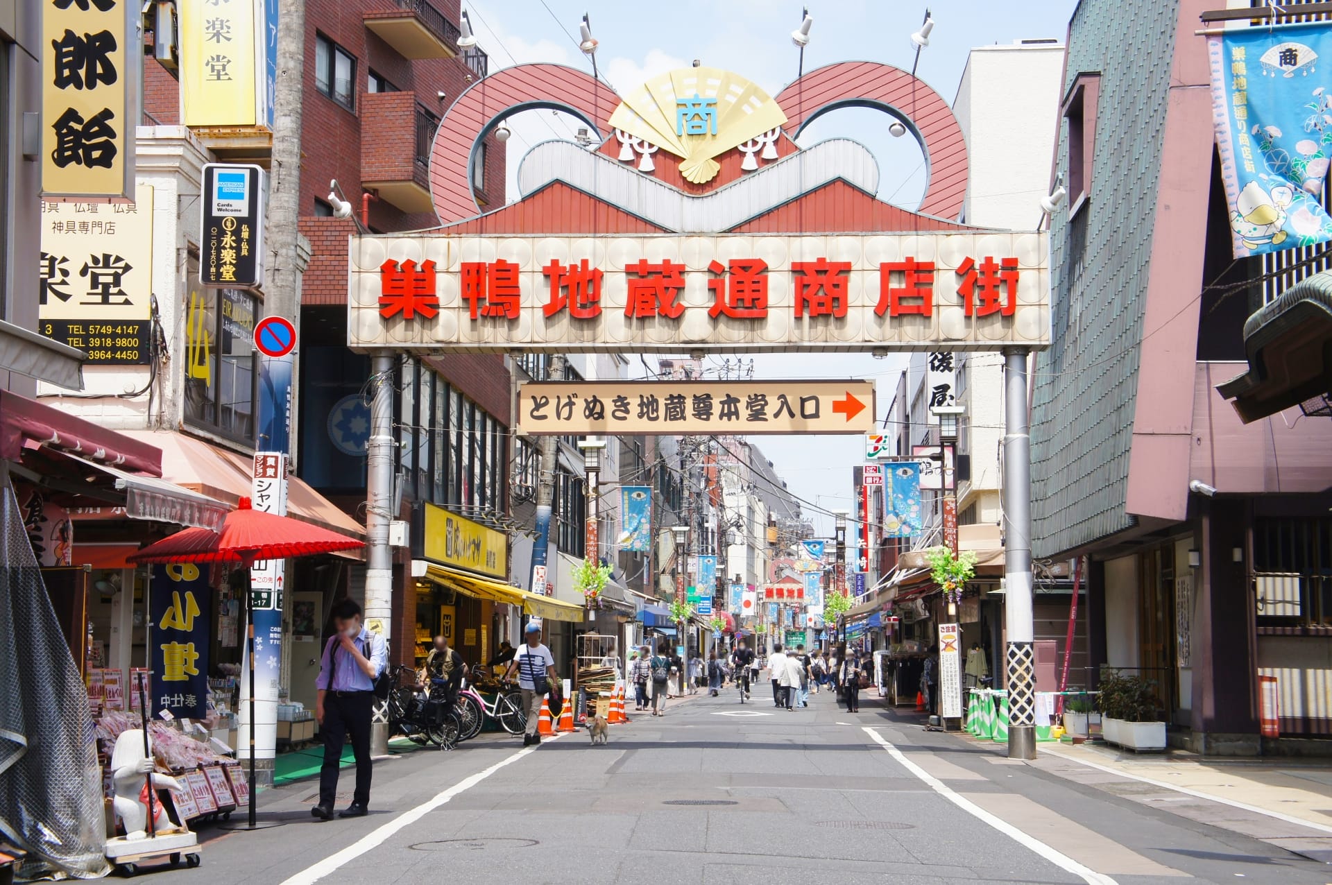 日本の巣鴨地区にあるにぎやかな通りには、頭上に大きな看板があり、その両側に複数の店が並んでいます。歩いたり自転車で通り過ぎたり、近くの韓国語教室マンツーマンのセッションに向かう人もいた。.