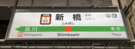 多言語で「新橋」を表示し、品川と東京への方向を示す駅看板。近くには、個人に合わせた韓国語レッスンを提供する韓国語教室マンツーマンがあります。.