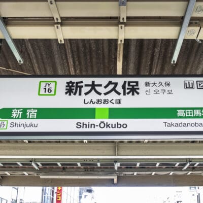 人気の韓国語教室マンマンクラスの近くのにぎやかな拠点である東京の新大久保の駅標識には、新宿と高田馬場への行き方が表示されており、駅コード JY16 が付いています。.