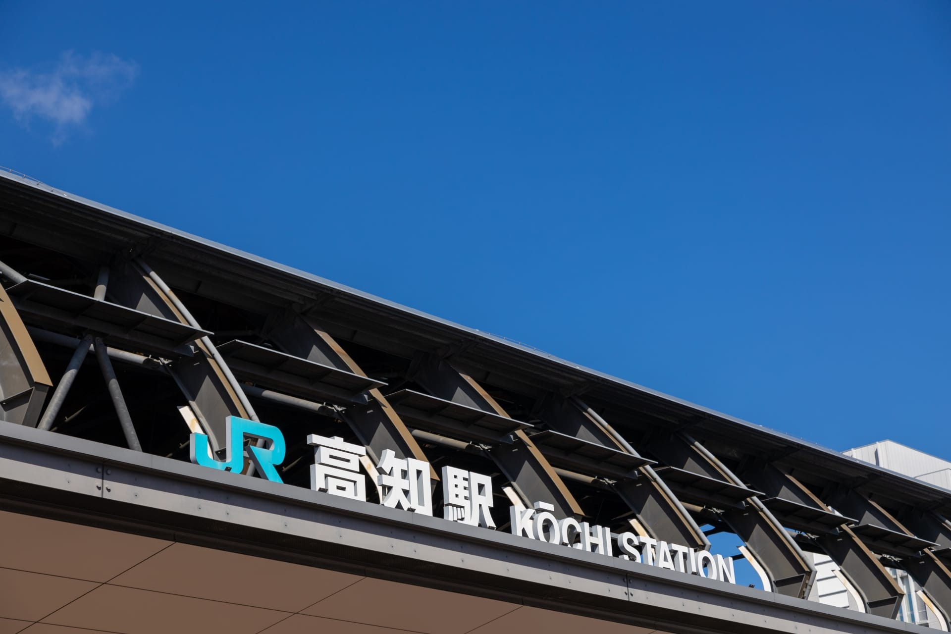 澄み切った青空を背景に、高知でマンツーマンで行われている韓国語の授業と同じように、日本語と英語の両方の文字が書かれた JR 高知駅の看板が誇らしげに立っています。.