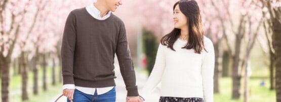 桜並木を手をつないで歩き、見つめ合って微笑む男女。.