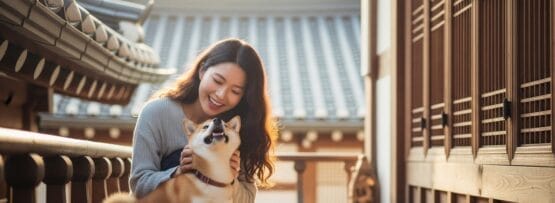 アジアの伝統建築を背景に、木造のベランダで柴犬を撫でながら微笑む女性。.