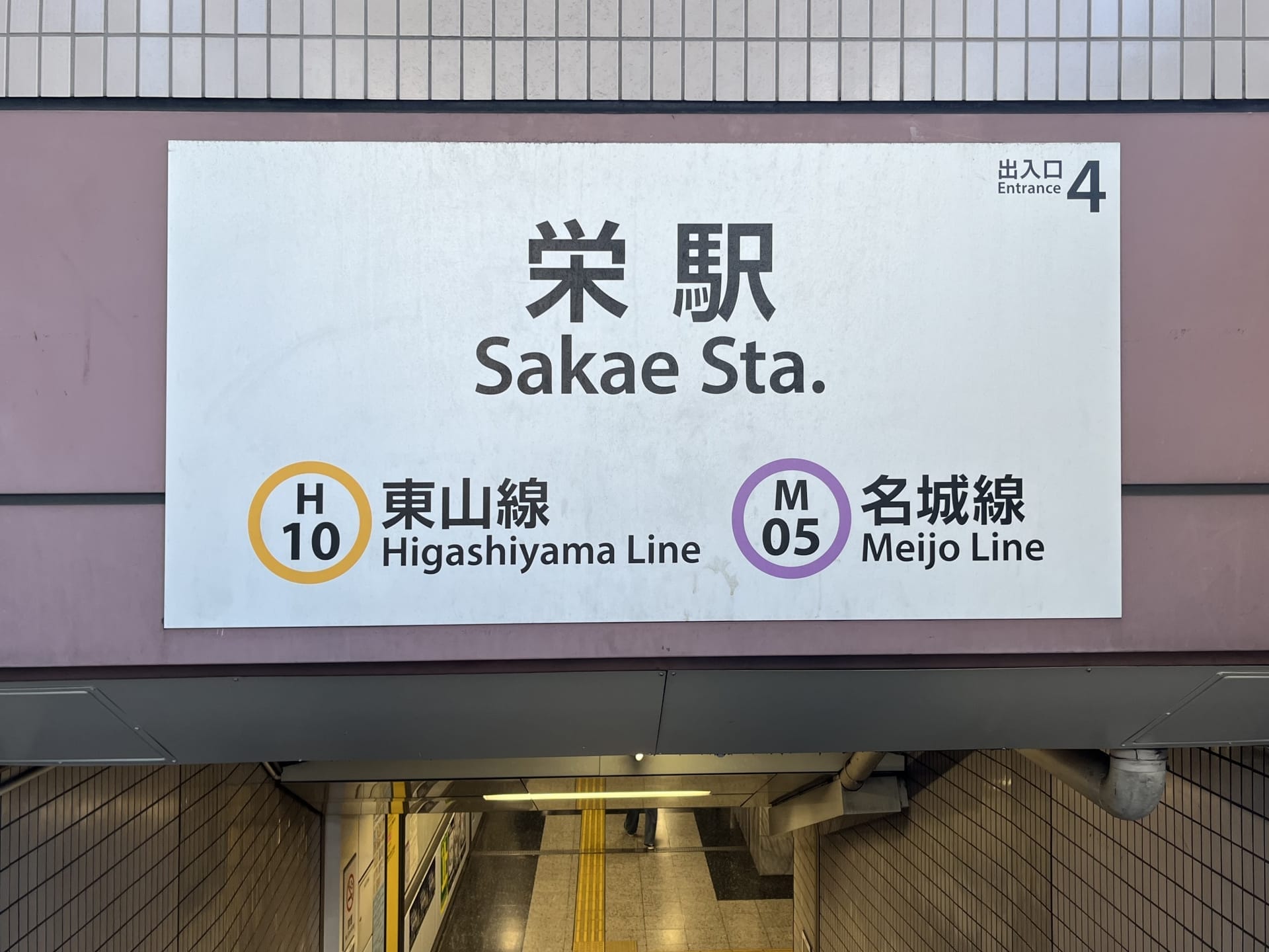 地下鉄入り口の上にある看板には「栄駅」と書かれ、東山線（H10）と名城線（M05）のマークがあり、4番出入り口を示している。.