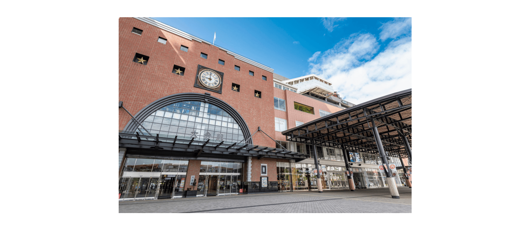 レンガ造りの建物で、入り口の上には大きな時計、下にはガラス戸、正面には屋根付きの歩道がある。.