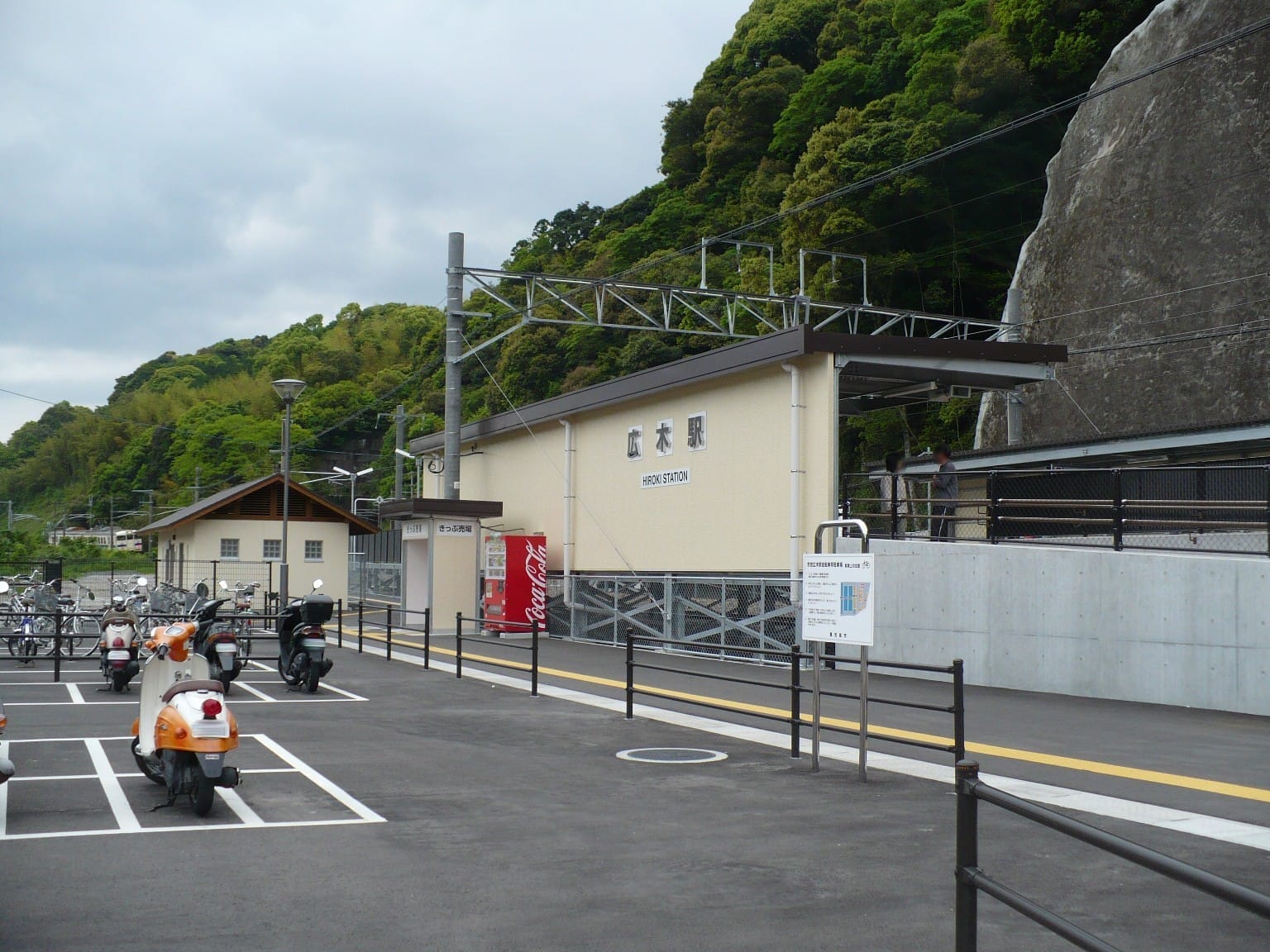 駐車場、オートバイ、自動販売機がある東金沢駅の駅舎。.