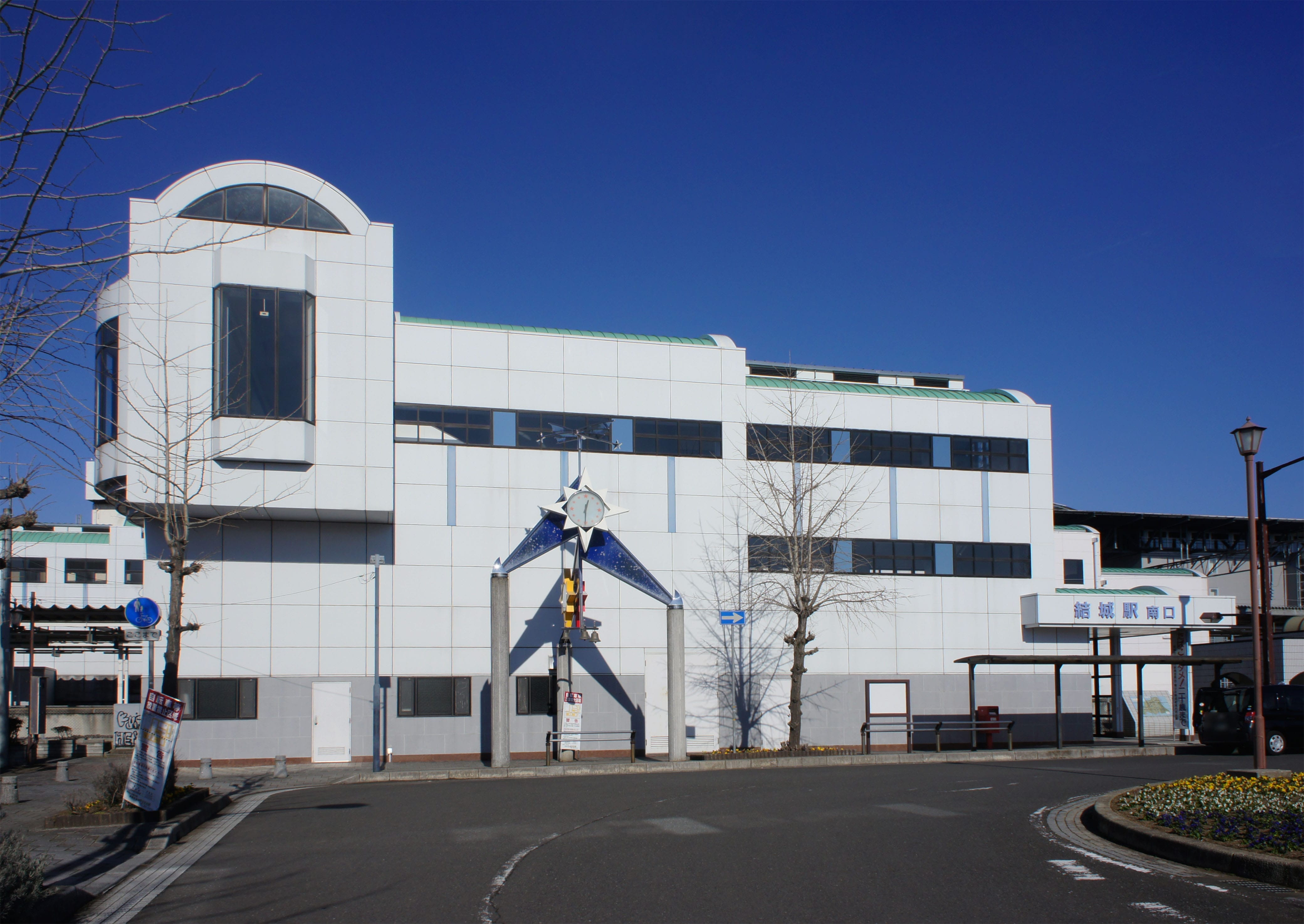 2階建てのモダンな白い建物には大きな窓があり、入り口には時計が設置され、正面には屋根付きの歩道がある。.