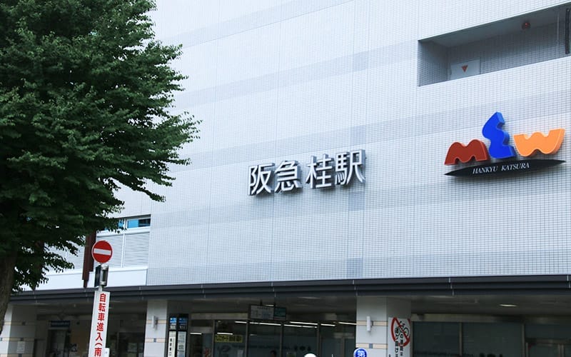 阪神桂駅の外観。駅舎には日本語の駅名、右側にはカラフルな「mw」のロゴ。.