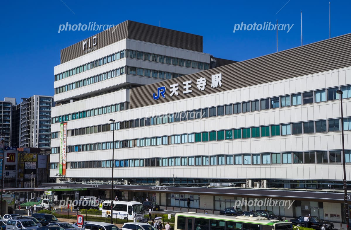 晴れ渡った青空の下、「JR天王寺駅」をはじめとする日本語の看板が掲げられた高層ビルが建ち並び、前方にはバスや車が走っている。.